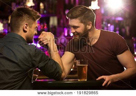 happy male friends drinking draft beer and arm wrestling at bar or pub
