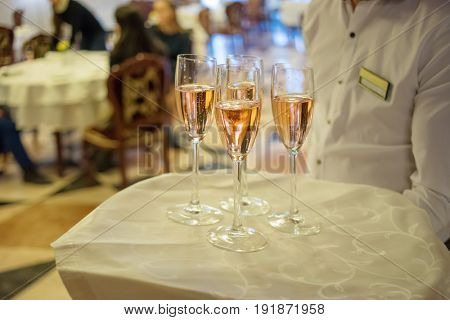Waiter holds tray with white sparkling wine during event, noface, people out of focus