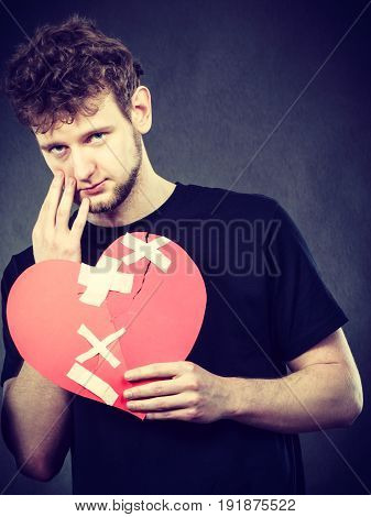 Heart broken concept. Unhappy sad man guy holding glued on love sign symbol. Human feeling repared by plaster. Valentines Day.