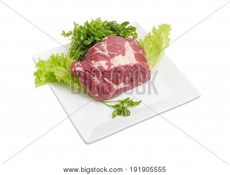 Piece of a fresh uncooked pork neck on the lettuce leaves and bundle of the parsley on the white square dish on a light background