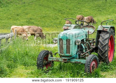 Old tractor on a meadow with fresh grass. Beautiful view to alpine mountains. Alps.