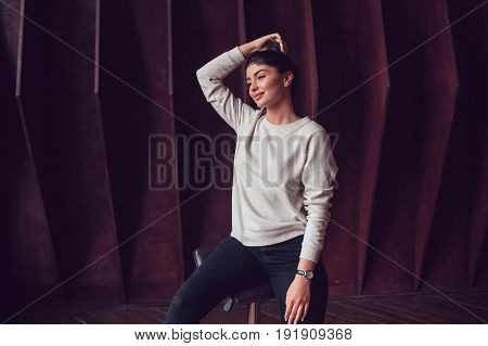 Attractive brunette woman in a grey sweatshirt stands on a dark wooden wall background. Mock-up.