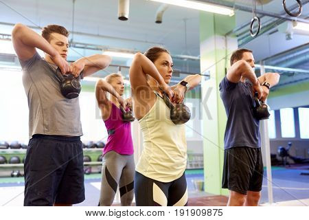 sport, fitness, weightlifting and training concept - group of people with kettlebells and heart-rate trackers exercising in gym