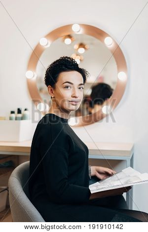 Attractive woman primp at the mirror with lamps in the beauty studio. A happy satisfied customer of make-up and hairstyle service.