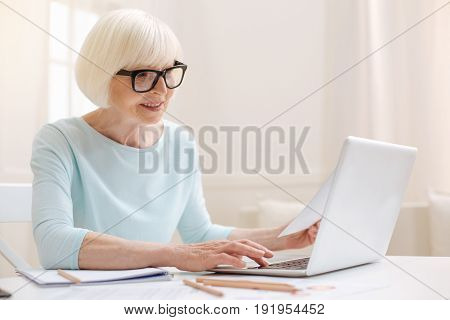 Aged expert. Cheerful productive ambitious woman working on her review of the article she reading while typing it on her computer