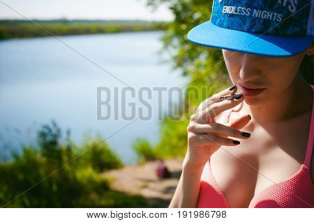 Young Sexy Woman In Swimsuit In Snapback On Her Head, Smokes Cigarette, Resting, Enjoying Summer On