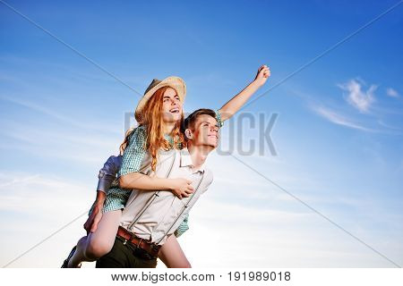 Young Man Piggybacking His Happy Girlfriend With Raised Hand. Cheerful Lovers Dreaming