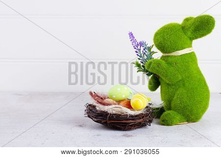 Easter Scene With Colored Eggs In Nest And One Green Bunny, Copy Spce Over Neutrl Bckground