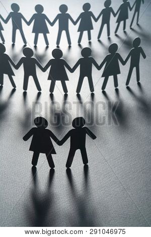 Black paper figure of a couple in front of a crowd of paper people holding hands on white surface. Social movement, protest, leadership concept.