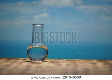 Clean water in a glass laboratory flask on wooden table on blue sea background. Ecological concept, the protection of water resources, the test of purity and quality of water.