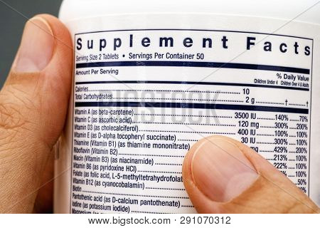 Close-up Of White Plastic Jar With Supplement Facts Of Multivitamins In Woman Hands.