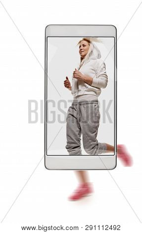 Portrait Of Young Sporty Woman Running On White Background. Conceptual Image With A Smartphone, Demo