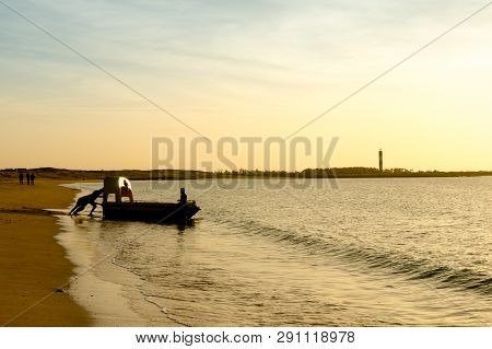 Silhouette Of Men Pushing A Tourist Fishing Boat Into The Ocean At A Gujarat Beach