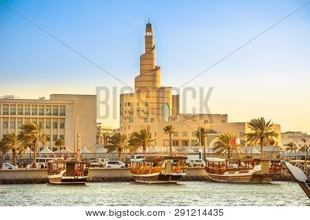 Traditional Wooden Dhow Anchored At Dhow Harbor In Doha Bay With Spiral Mosque And Minaret In The Ba
