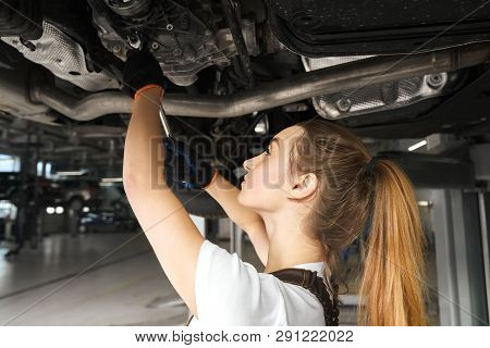 Young Woman Holding Tool, Fixing Car. Girl Working Undercarriage Of Automobile, Auto Lifted On Bridg