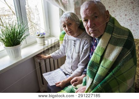 The Senior Woman Holding Gas Bill In Front Of Heating Radiator. Payment For Heating In Winter.