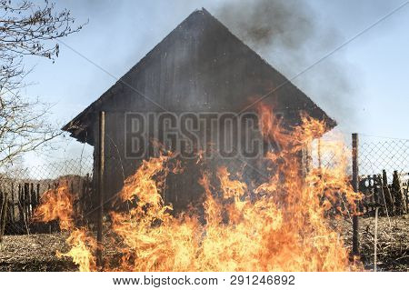 Burning Grass. Fire Outdoors. Behind The Wooden House