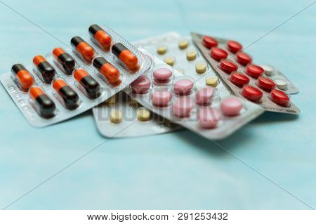 Multicolored Pills And Capsules In Blisters Close-up, On Blue Background. The Concept Of Treating Hu