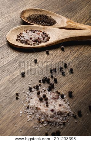 Two Wooden Spoons With Salt And Pepper On A Wooden Table