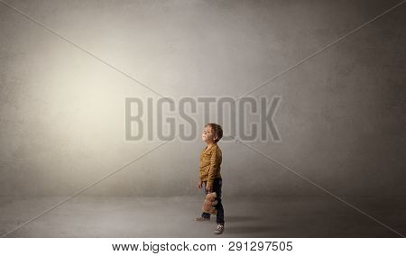 Little waggish kid staying alone in a big empty room with his plush