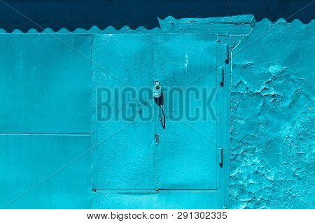 Closed Imperfect Blue Garage Gate With Padlock Close-up. Texture Of Locked Iron Door With Cyan Peeli