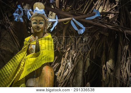 A Wooden Statue Of A Praying Or Meditation Spirit Of Trees, Girl. Tree With White Ribbons. Thai Gree