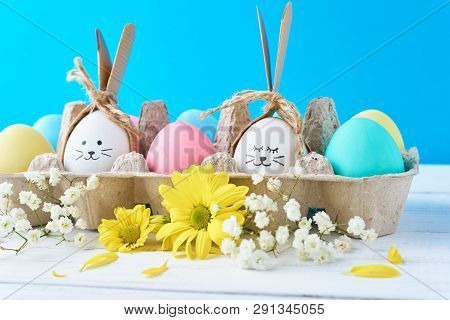 Easter Colored Eggs In Paper Tray With Decorationd On Blue Background