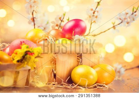 Easter colorful eggs in the basket. Beautiful colorful yellow and orange color eggs with decorations and spring flowers over bright blurred bokeh background.