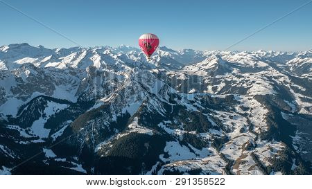 Rougemont, Switzerland -  03 21 2019: 

A Hot Air Balloon In Flight Over The Snow Covered High Mount