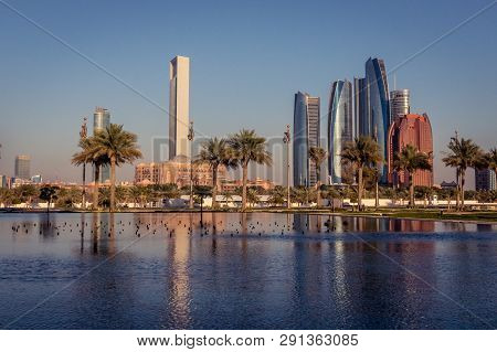 Abu Dhabi Skyline At Golden Hour. Skyscrapers Reflecting In The Garden Lakes. View On Emirates Palac