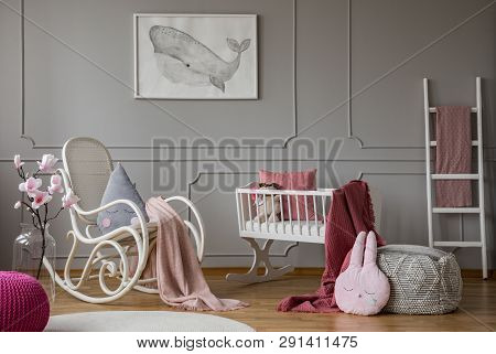 Flowers And Rocking Chair In Grey Baby's Bedroom Interior With Poster And Pouf. Real Photo