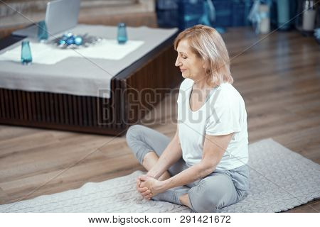 Adult Woman Does Yoga At Home. In Asana Position She Sits On The Floor. After Practicing Yoga She Me