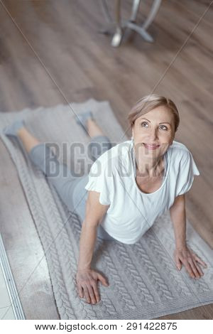 An Adult Woman Likes To Do Yoga At Home. She Is In The Position Of Asana On The Floor In The Living 