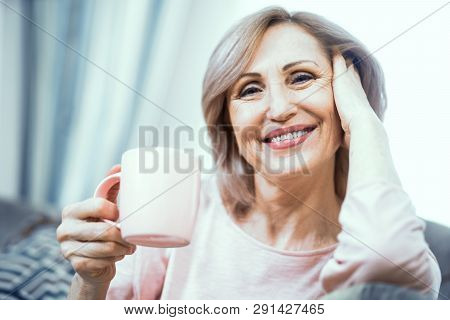 A Woman Over 50 Years Of European Appearance Resting At Home Drinking Coffee. The Woman Smiles Broad
