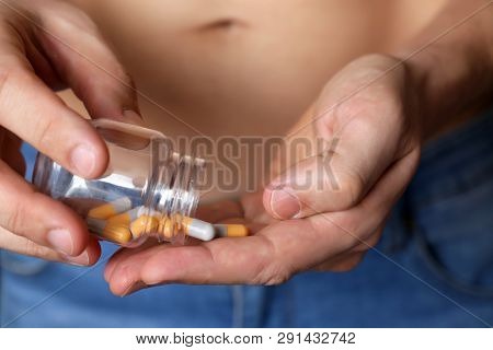 Man Taking Pills, Bottle With Capsules In Male Hands Close Up. Guy In Unzipped Jeans With Naked Tors