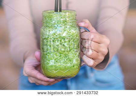 Woman Hand Holding Smoothie Shake In Front Of Her. Drinking A Healthy Green Smoothie Concept.
