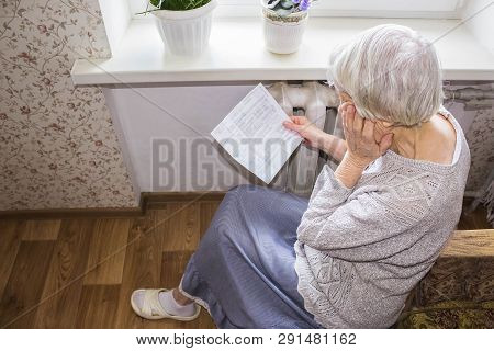 The Senior Woman Holding Gas Bill In Front Of Heating Radiator. Payment For Heating In Winter.