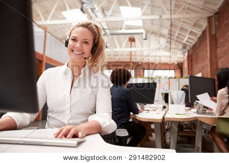 Portrait Of Female Customer Services Agent Working At Desk In Call Center