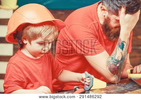 Educational Games Concept. Boy, Child Busy In Protective Helmet Learning To Use Handsaw With Dad. Fa