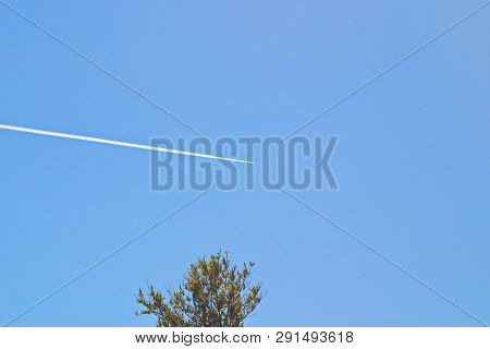 Image Of The Inversion Trace Of A Combat Aircraft In The Blue Sky Above The Trees