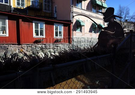 Vasteras, Sweden - 22 March, 2019: Small sculpture boy fishing on Svartan with swedish style red wooden houses on backdrop