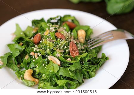 Spinach Salad With Seeds, Nuts And Sunflower Oil In Pottery On A Light Wooden Background With Space 