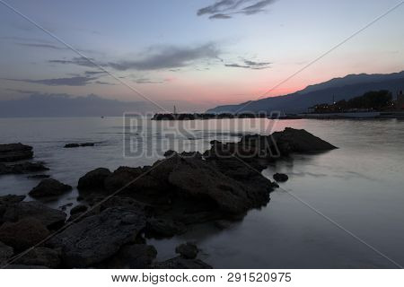 Pink And Blue Sunset On The Beach In Creta, Greece. Beach With Blacks Rocks And Waves At Dusk