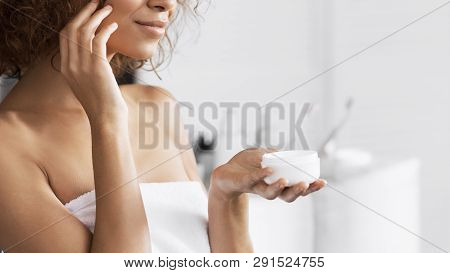 Beautiful Afro Girl Holding Cream Jar, Standing In Bathroom. Professional Cosmetics For Beautul Skin