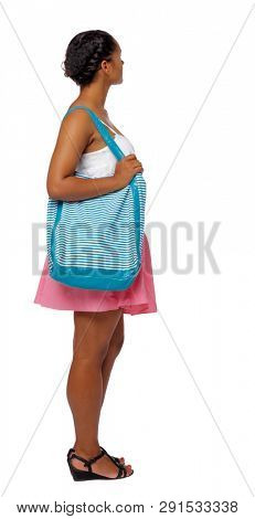 Side view of a young African-American with a beach bag girl  watching. Rear view people collection.   Isolated over white background. A black girl with bag on her shoulder is looking sideways.