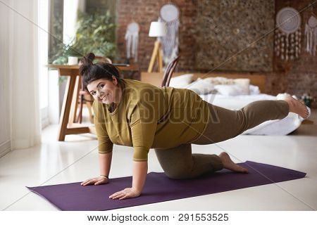 Cheerful Self Determined Young Woman With Curvy Body And Hair Knot Exercising Indoors On Yoga Mat St