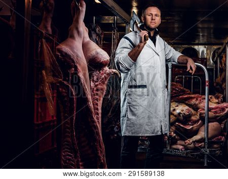 The Butcher In A White Work Shirt Holding Ax While Standing In A Refrigerated Warehouse In The Midst