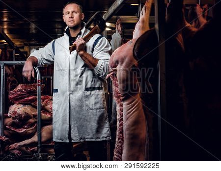 The Butcher In A White Work Shirt Holding Ax While Standing In A Refrigerated Warehouse In The Midst