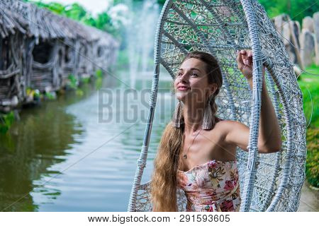 Beautiful Brunette In Dress Swinging On A Swing Over The Water In The Park In Sunny Day