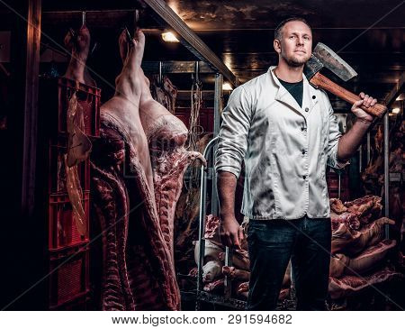 The Butcher In A White Work Shirt Holding Ax While Standing In A Refrigerated Warehouse In The Midst